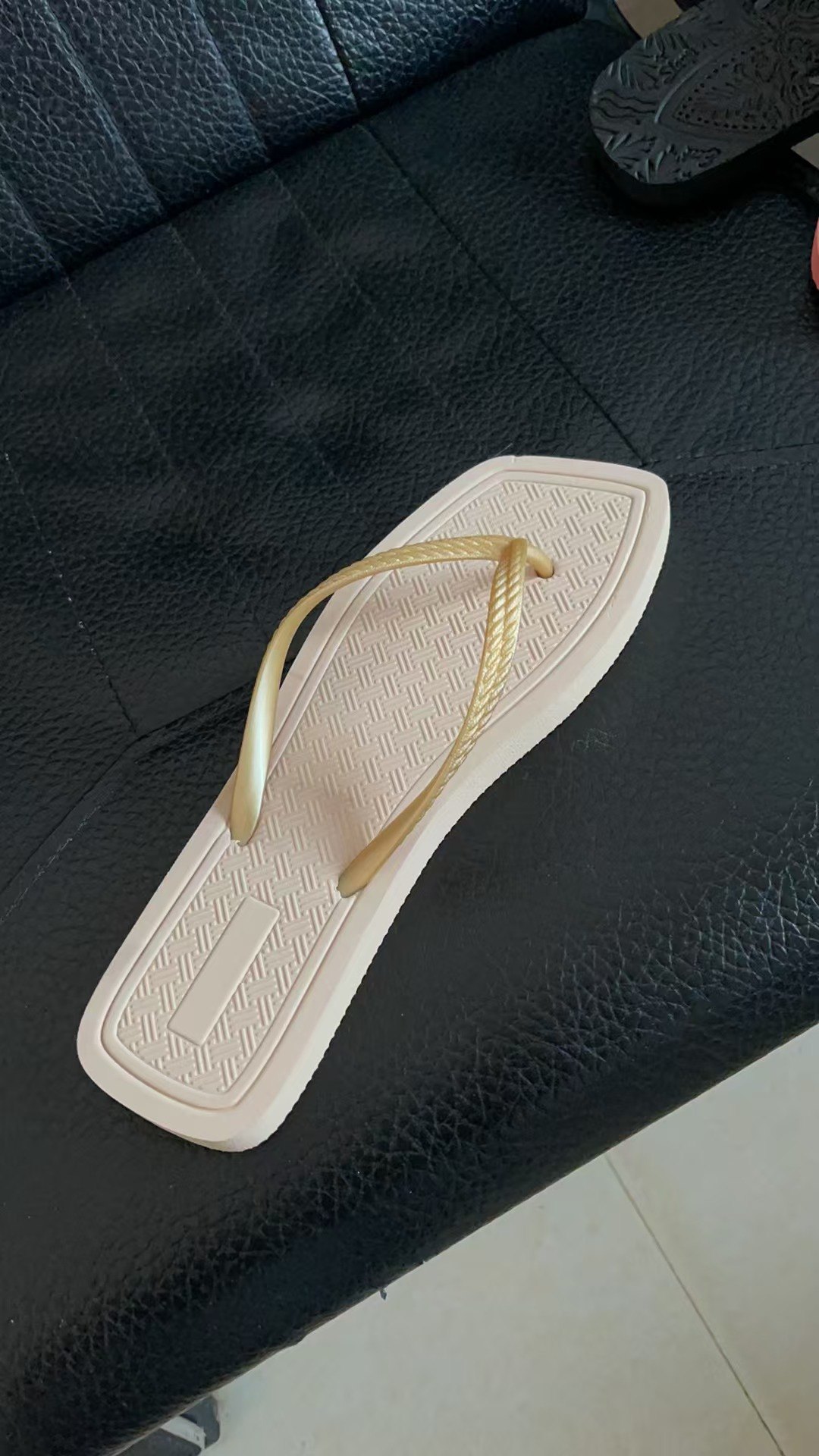 图片展示了一只露指鞋,放置在黑色皮质沙发上。鞋子为浅色,鞋带为金属质感,鞋底有纹理设计。图片位于“商品图”部分,是可选择的露指鞋商品图之一,用于展示商品外观。上下文提到可选择侧面上脚方向的穿戴姿势图进行穿戴,此图可作为商品图参考。