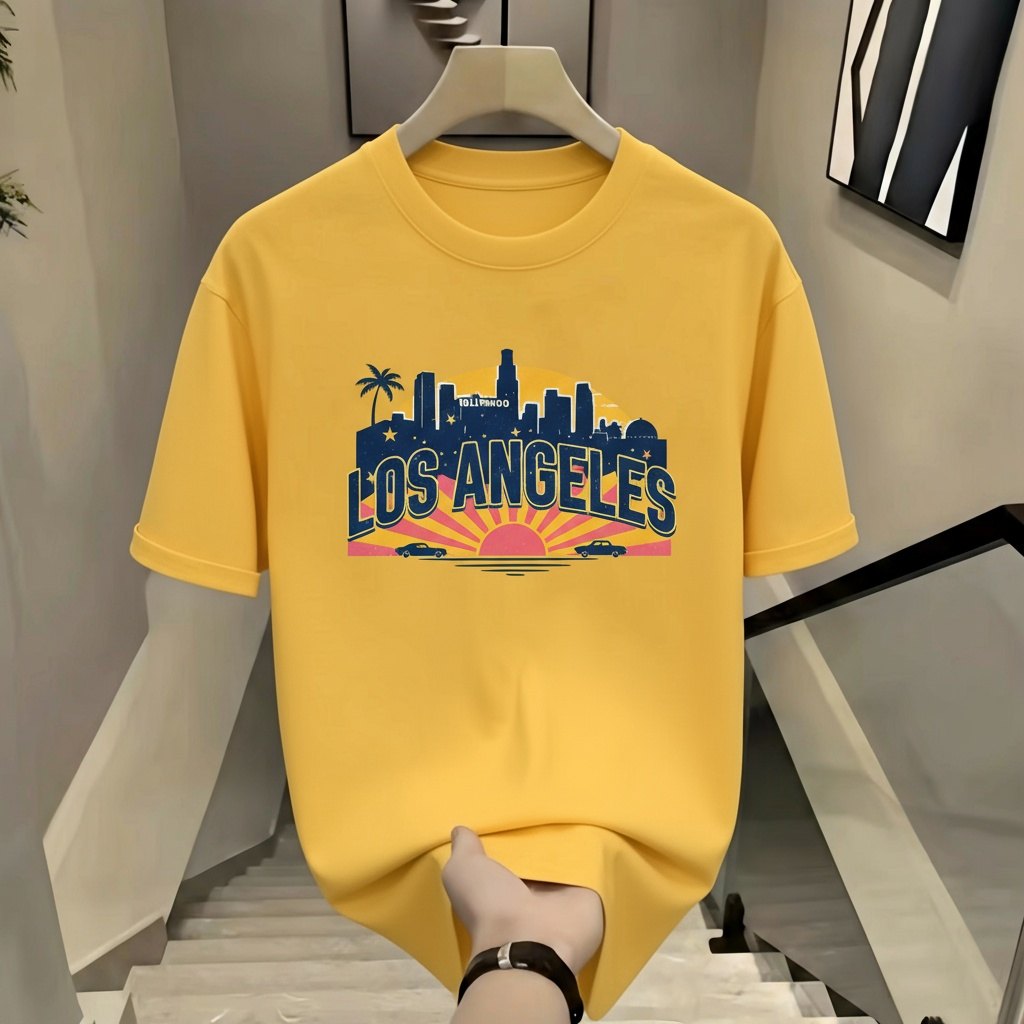 图片展示了一件黄色T恤，T恤正面印有“LOS ANGELES”字样及城市剪影图案，背景为日落景象。T恤被模特手臂撑开，模特手部戴有黑色手环。T恤放置在带有黑色扶手的楼梯上，背景墙面为浅色，挂有黑白相间的装饰画。此图对应文档中“修改商品款式/形状”场景下的示例，提示词为“将上衣改为V领短袖款式，保留上衣原有的橙色”。
