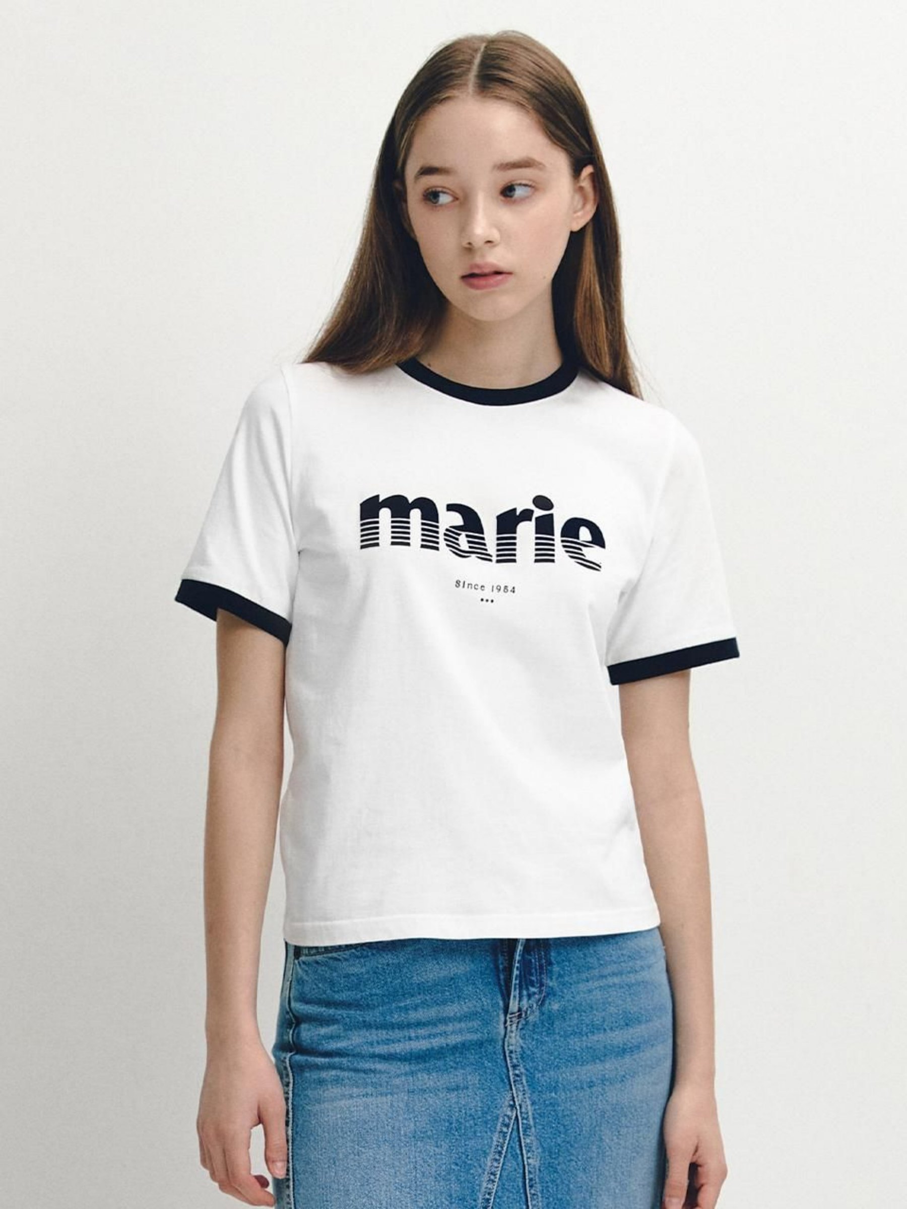 图片展示了一位年轻女性的原图。她身着一件白色T恤，T恤上有“marie”字样及“since 1982”等文字，T恤袖口和领口有黑色边。她穿着蓝色牛仔裤，头发为棕色长发，面带微笑，背景为纯白色。该图片位于“修改商品款式/形状”案例中，用于说明将上衣改为V领短袖款式，保留上衣原有橙色的使用场景。